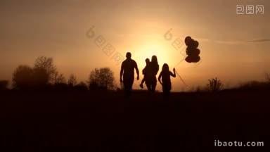 草地后视图中幸福家庭的剪影和孩子们走进夕阳的余晖中